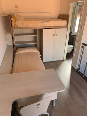 Un lit superposé avec un bureau en dessous, une armoire et une salle de bain à l’arrière-plan.