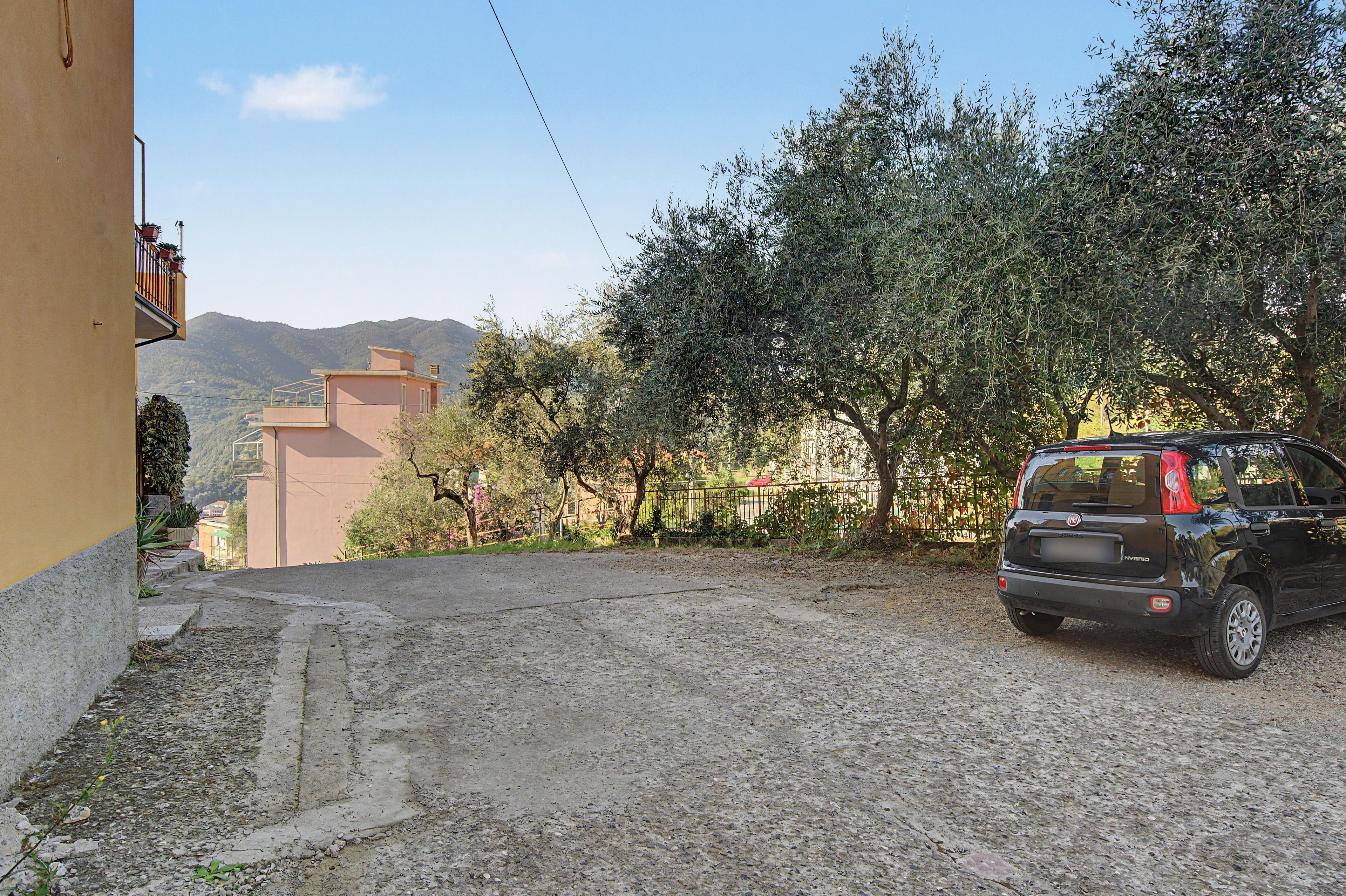 A residential area with a paved driveway, a parked car, and a building with a balcony.
