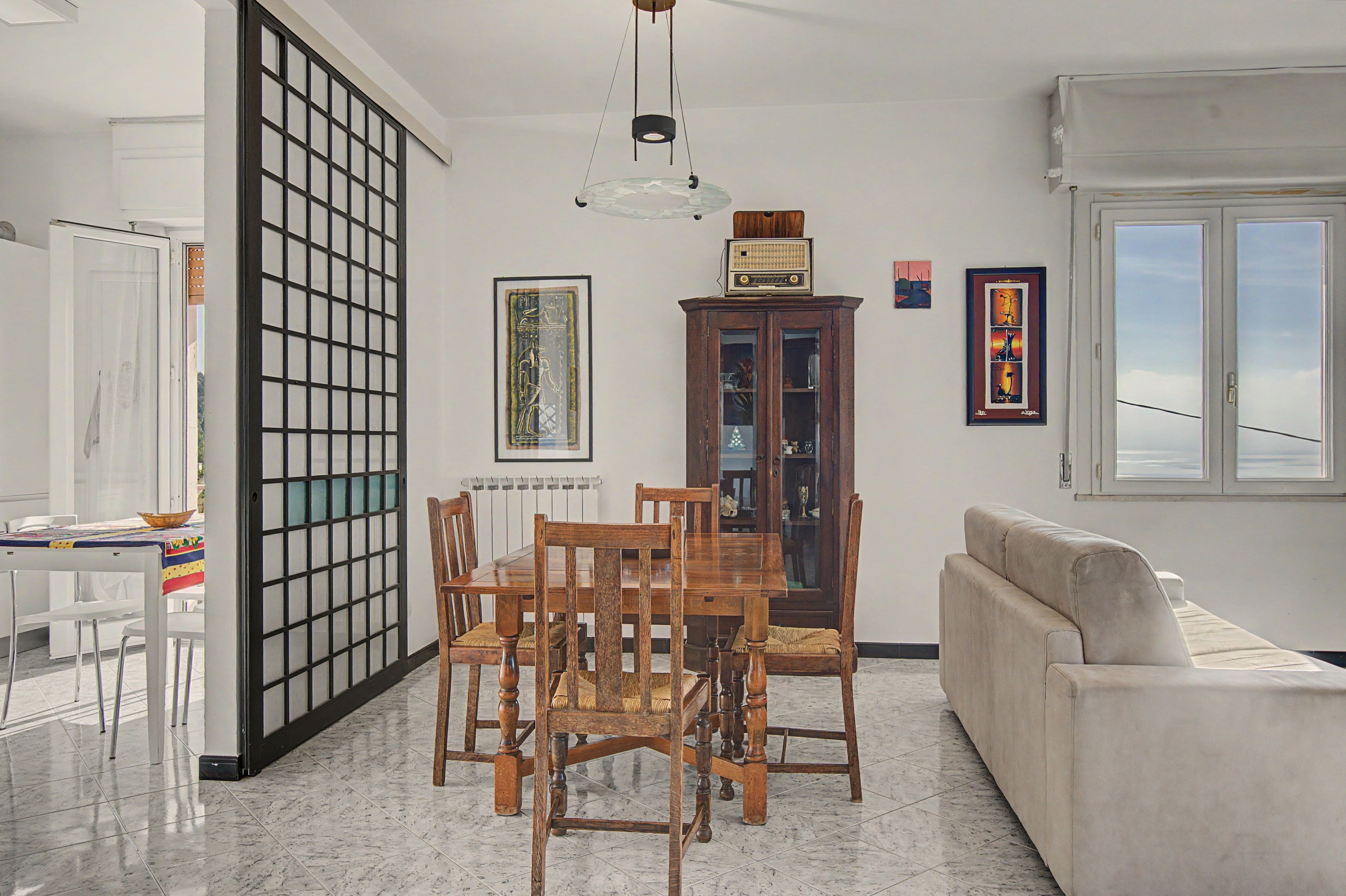 A dining area with a wooden table and chairs, a cabinet with glass doors, and a white sofa.