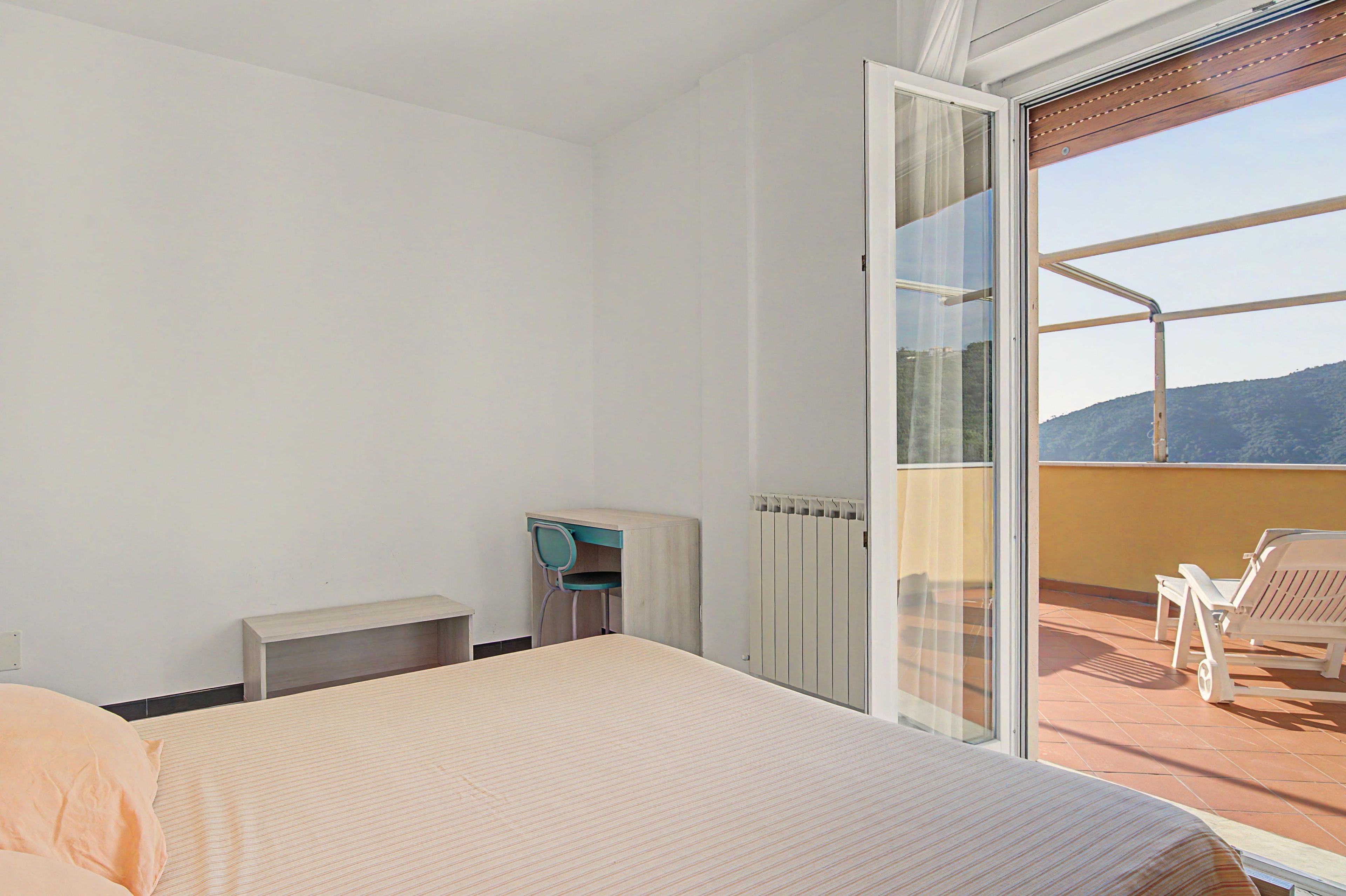 A hotel room with a bed, a small table, a chair, and a view of the outdoors through a sliding glass door.