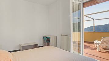 A hotel room with a bed, a small table, a chair, and a view of the outdoors through a sliding glass door.