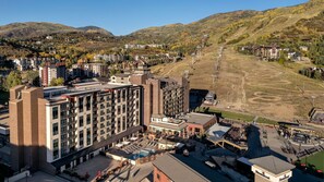 Ein mehrstöckiges Hotel mit Poolbereich auf dem Dach, umgeben von einer hügeligen Landschaft.