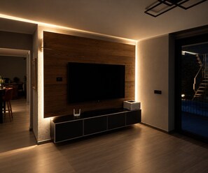 A modern living room with a flat-screen TV mounted on a wooden wall, a built-in entertainment unit below, and a staircase leading to an outdoor area. - Il Riparo – Silence and Luxury in the Mountains (Le Lou)