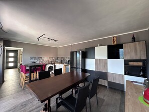 A modern kitchen with a dining area, featuring a wooden table, chairs, and a built-in oven. - Il Riparo – Silence and Luxury in the Mountains (Le Lou)