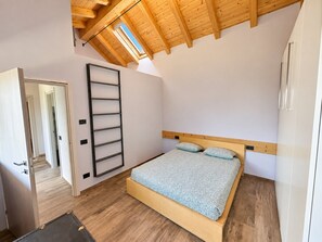 A bedroom with a wooden ceiling, a bed with a headboard, a ladder, and a door leading to another room. - Il Riparo – Silence and Luxury in the Mountains (Le Lou)