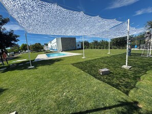 Un jardí ben cuidat amb una piscina, un edifici blanc i una gran estructura de teulat blanc.