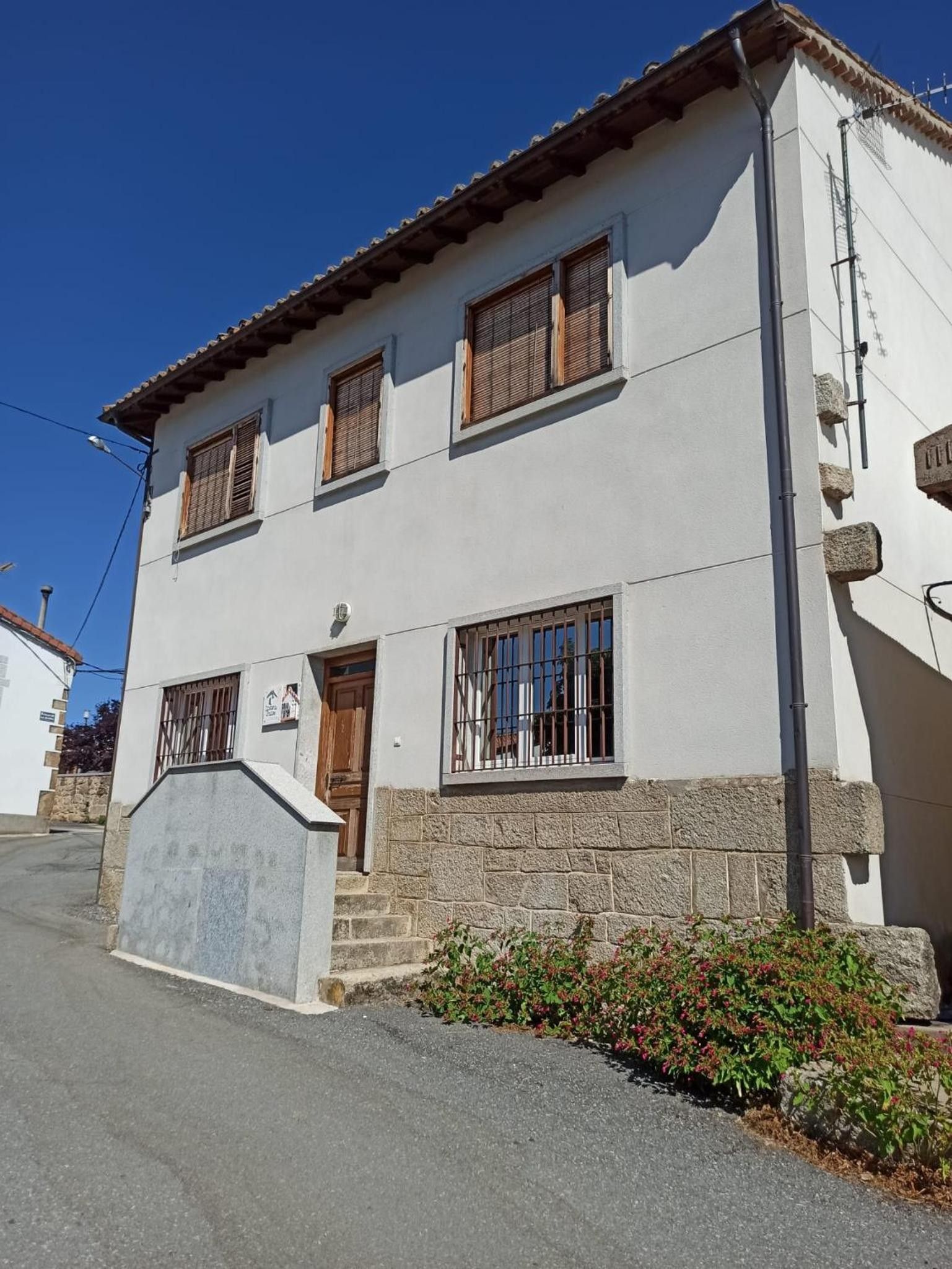 A two-story building with a stone base, wooden shutters on windows, and a small porch with steps.