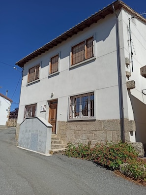 A two-story building with a stone base, wooden shutters on windows, and a small porch with steps. - Country House 'La Bimborra' (Becedas)