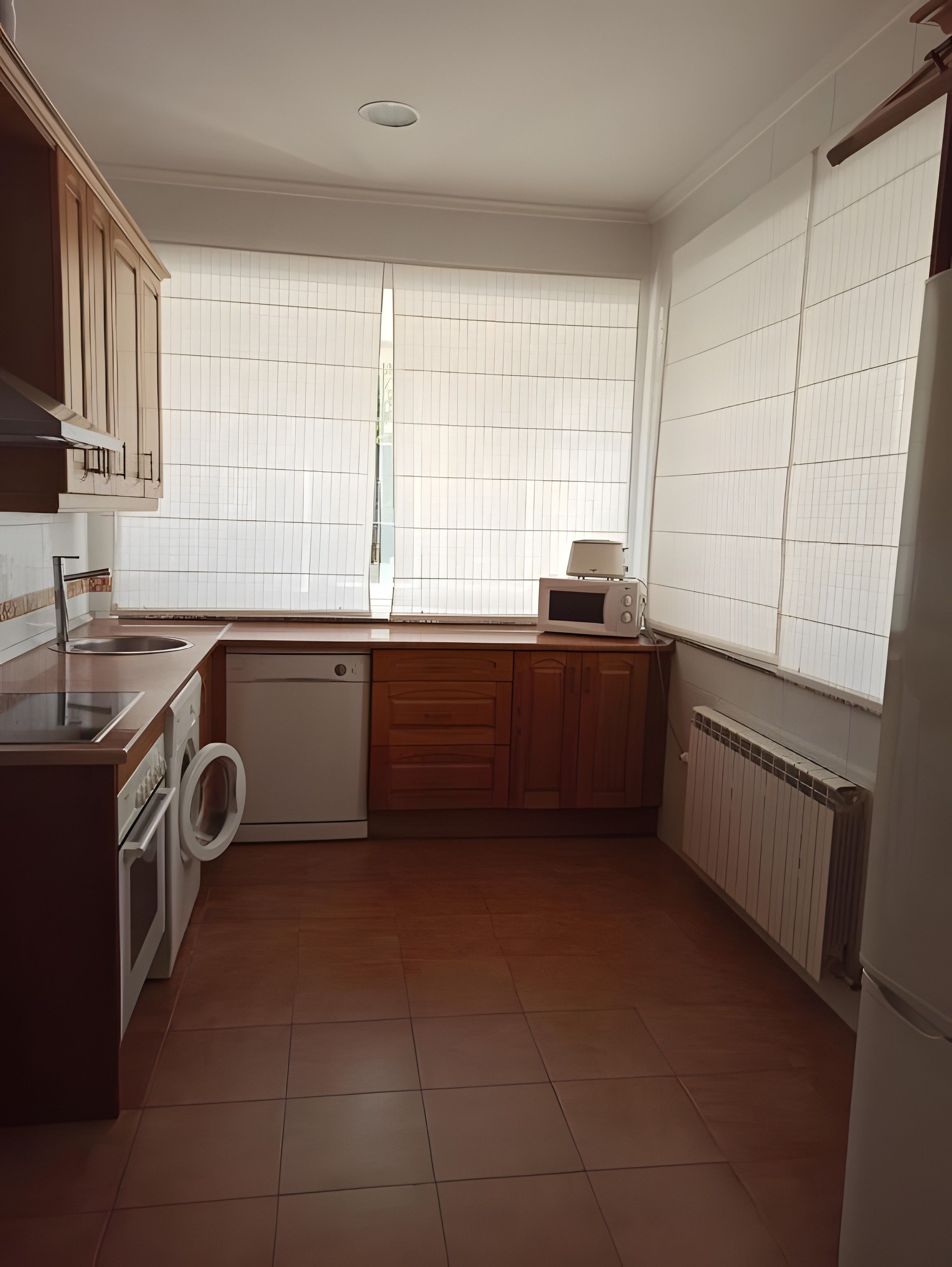 A kitchen with wooden cabinets, a built-in microwave, a dishwasher, and a window with blinds.
