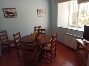 A dining area with a round table, six wooden chairs, and a vase with flowers. There are two framed pictures on the wall, a window with a view, and a radiator. - Country House 'La Bimborra' (Becedas)