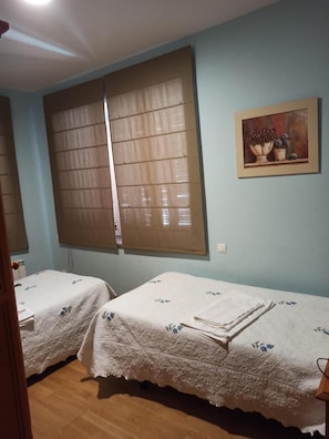 Una habitació amb dos llits, un quadre a la paret i una finestra amb persianes.