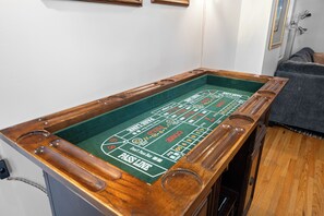 Ein Craps-Tisch mit grüner Spielfläche und Holzleisten, in einem Raum mit grauem Sofa und weißer Wand.