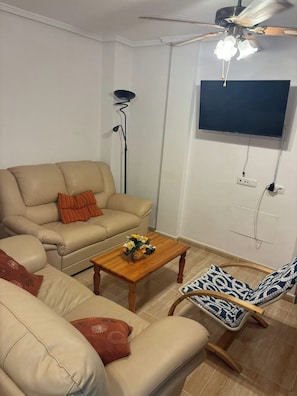 A living room with a sofa, a coffee table, a chair, a floor lamp, and a television mounted on the wall. - House Sleeps 4 - Air Con, Parking, Community Pool (San Fulgencio)