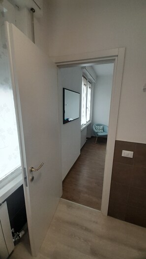Um corredor com uma porta que dá para um quarto, com uma cama e uma janela.
