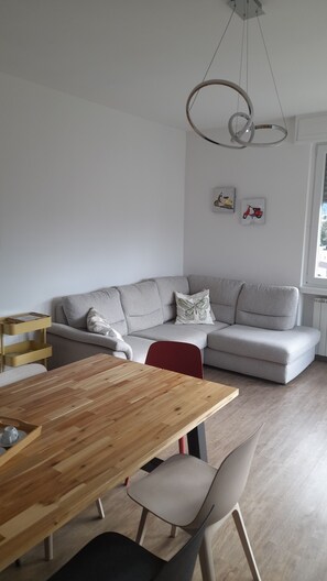 A modern living space with a wooden dining table, grey sofa, and a red chair. - Aurora Vacation Home: Between the Lake and the Mountains (Costa Volpino)