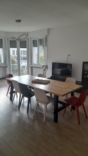 Uma sala de jantar com mesa de madeira, cadeiras, um ventilador e uma televisão.