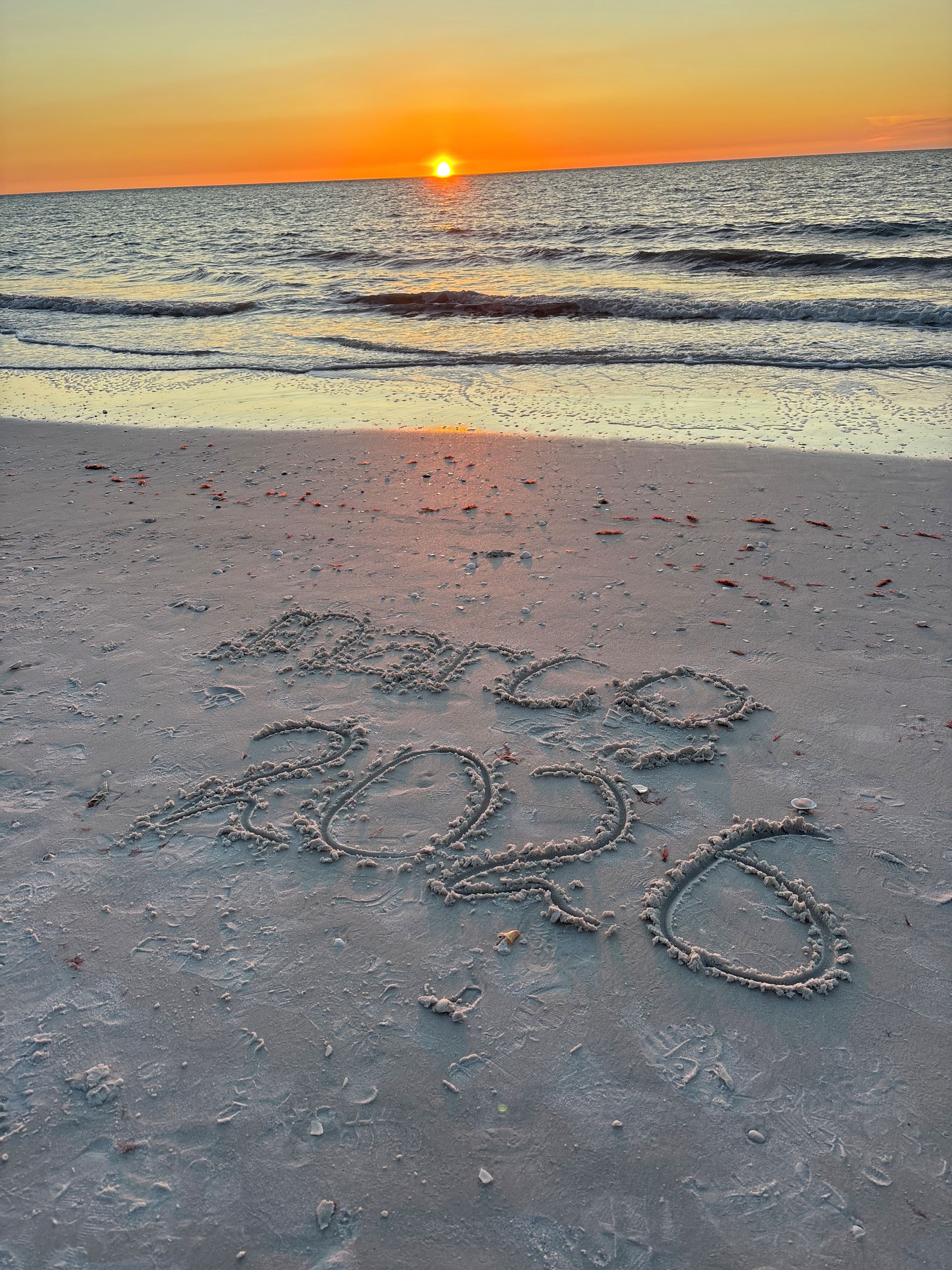 Una playa con huellas y el número 2020 escrito en la arena.