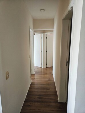 A hallway with wooden flooring and white walls, leading to a door at the end. - 3-bedroom apartment with ocean view and 2 covered parking spaces. (Florianópolis)