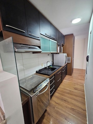 A modern kitchen with dark cabinets, a stainless steel range hood, a microwave, and a dishwasher. - 3-bedroom apartment with ocean view and 2 covered parking spaces. (Florianópolis)