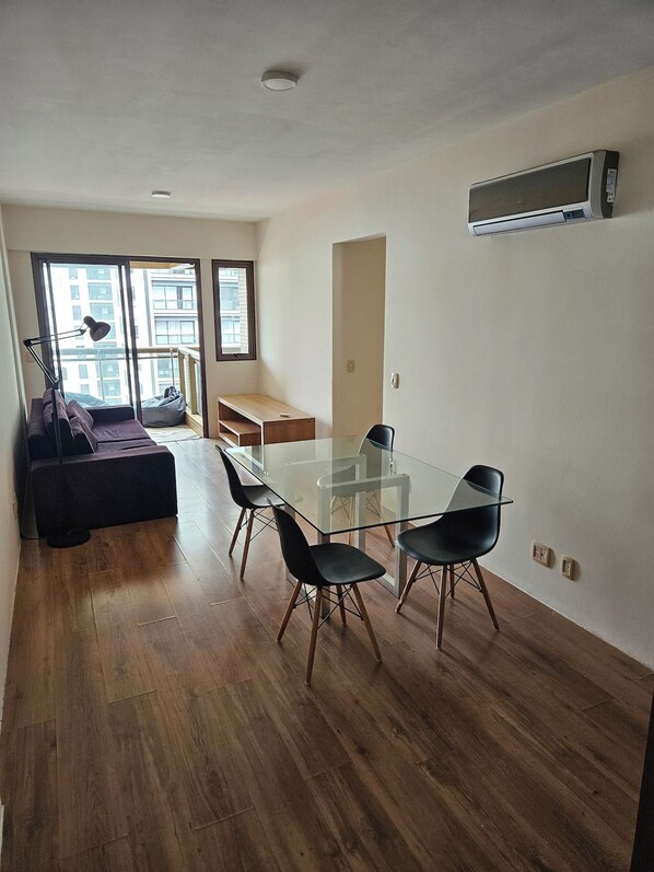 Una sala moderna con una mesa de vidrio, sillas negras, un sofá y un ventanal grande.