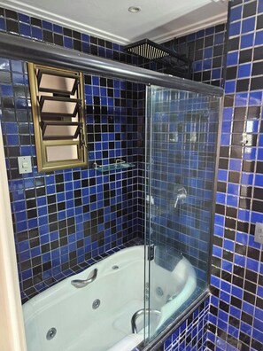 Un baño con ducha envuelta en vidrio, una bañera blanca y mosaicos azules oscuros en las paredes.