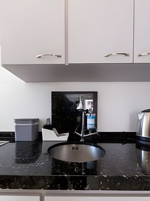 A modern kitchen with white cabinets, a black countertop, and a stainless steel sink. - Apartamento Espaçoso e Confortável (Rio de Janeiro)
