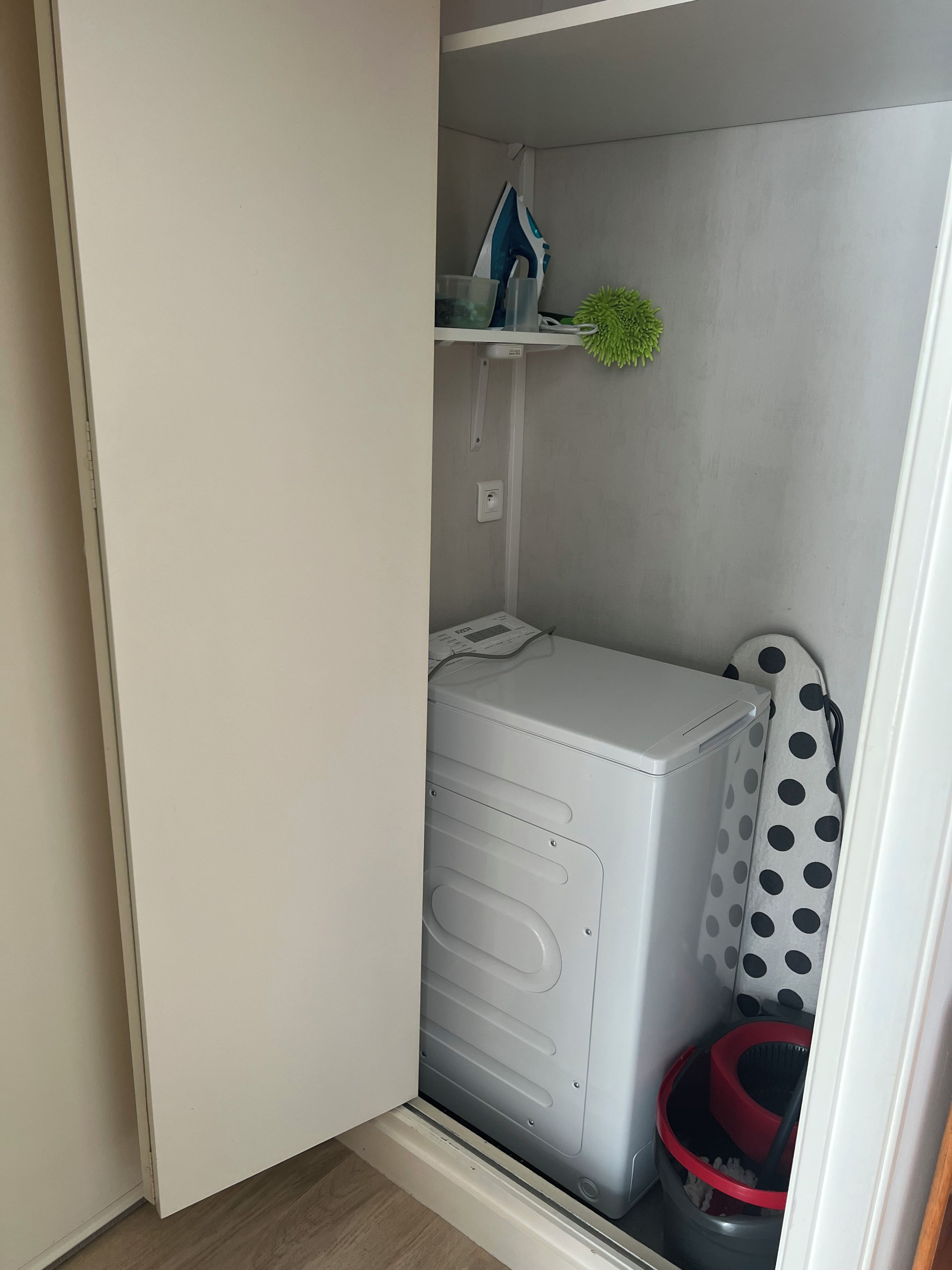 A compact laundry room with a washing machine, a drying rack, and a trash bin.