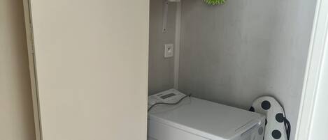 A compact laundry room with a washing machine, a drying rack, and a trash bin.