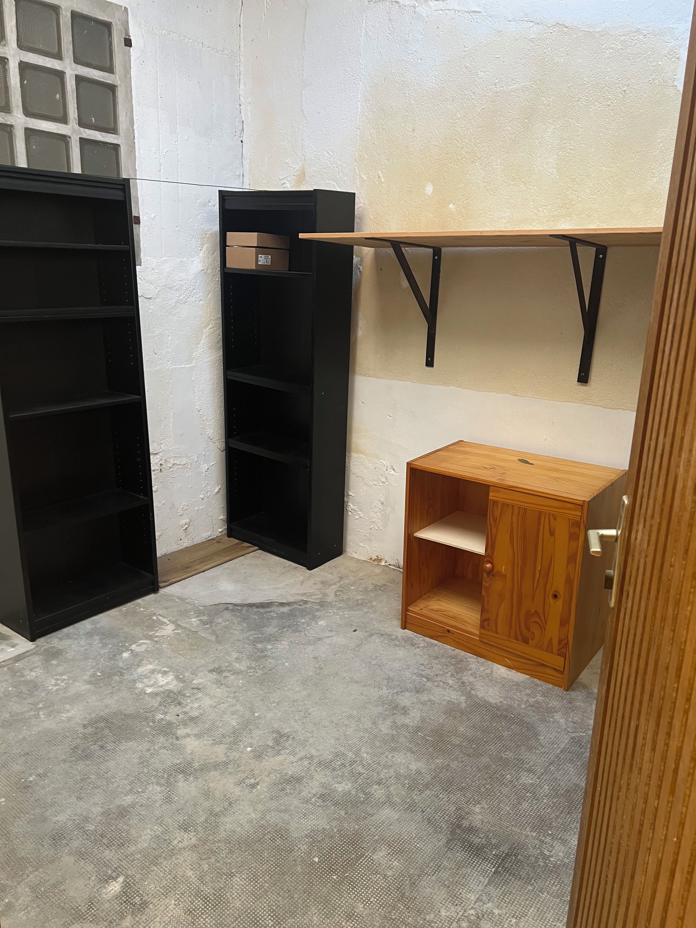 A room with a concrete floor, a black metal shelving unit, and a wooden cabinet with a door.