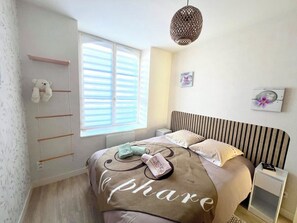 Ein Schlafzimmer mit einem Bett, einem Nachttisch, einem Fenster mit Jalousien, einer Pendelleuchte und einem Wandregal mit einem Teddybär.
