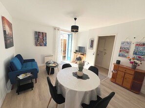 Ein Wohnzimmer mit einer Couch, einem Esstisch mit Stühlen, einem Fernseher und einer Tür zu einem anderen Raum.