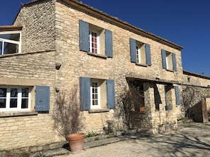 A stone building with multiple windows and shutters, a gravel driveway, and a potted plant. - The Bastide of the Valleys (Murs)