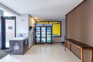 Corredor com máquina de vendas automática, geladeira e um banco.