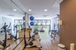 Academia com equipamentos de cardio, aparelhos de musculação e uma grande janela que proporciona iluminação natural.