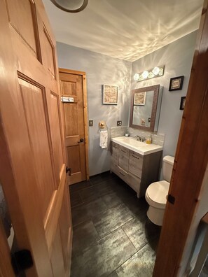 Ein Badezimmer mit Holztür, Waschbecken, Spiegel und Toilette.