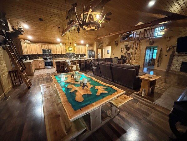 A spacious living area with a wooden floor, a central coffee table, a sofa, and a kitchen in the background.
