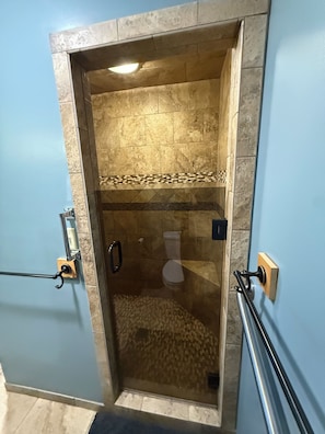 Un box de ducha con paredes de vidrio, piso de azulejos, barra de apoyo y toallero.