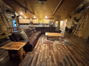 Ein geräumiger Wohnbereich mit einem großen, winkelförmigen Schlafsofa, einem Holztisch und einem Parkettboden mit Zickzackmuster.