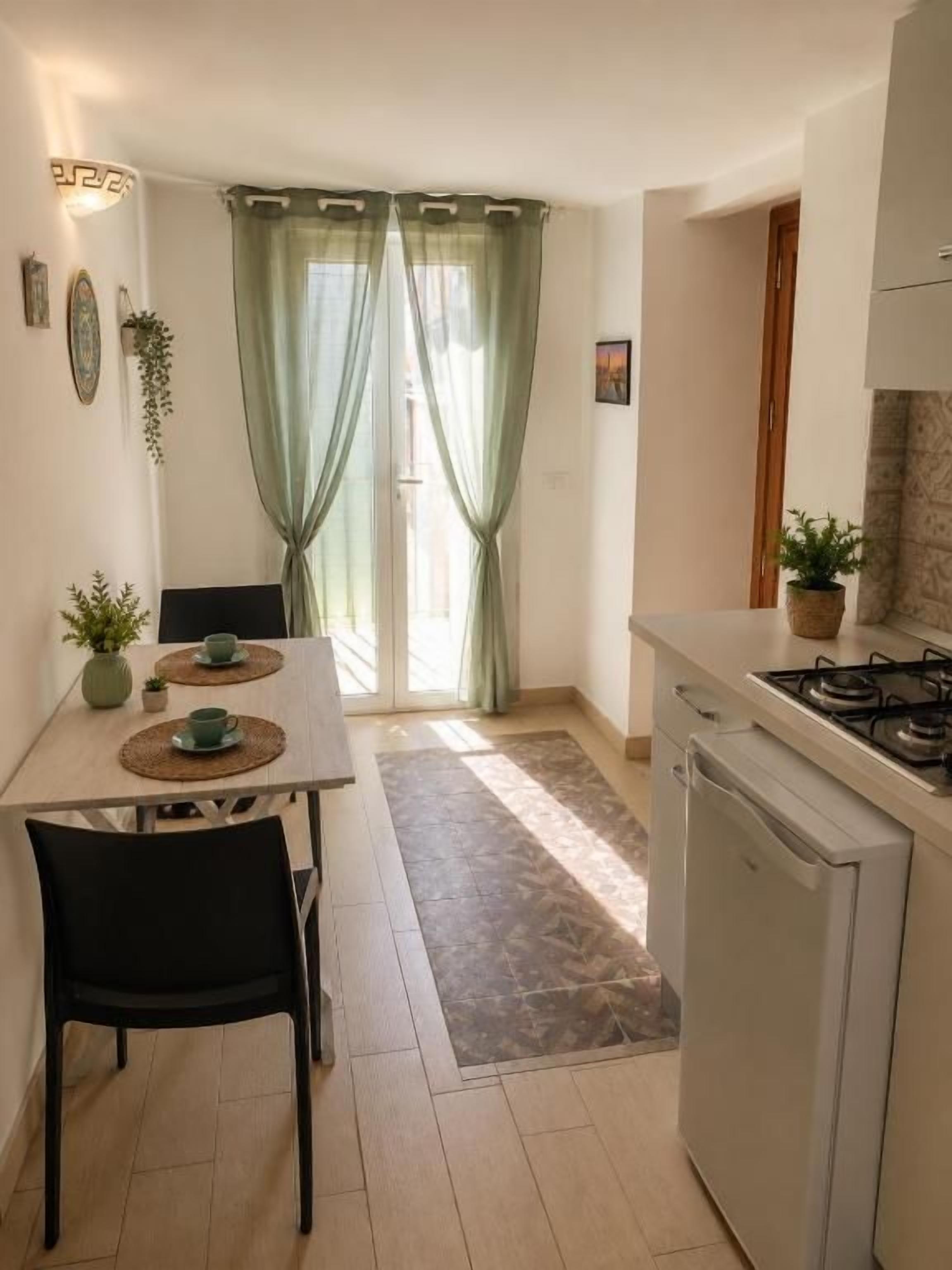 A compact kitchen with a dining table, chairs, a refrigerator, and a gas stove.