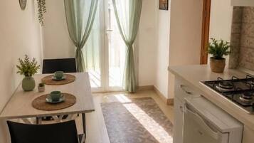 A compact kitchen with a dining table, chairs, a refrigerator, and a gas stove.