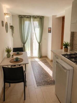 A compact kitchen with a dining table, chairs, a refrigerator, and a gas stove. - TELAMON HOME RENT (Agrigento)
