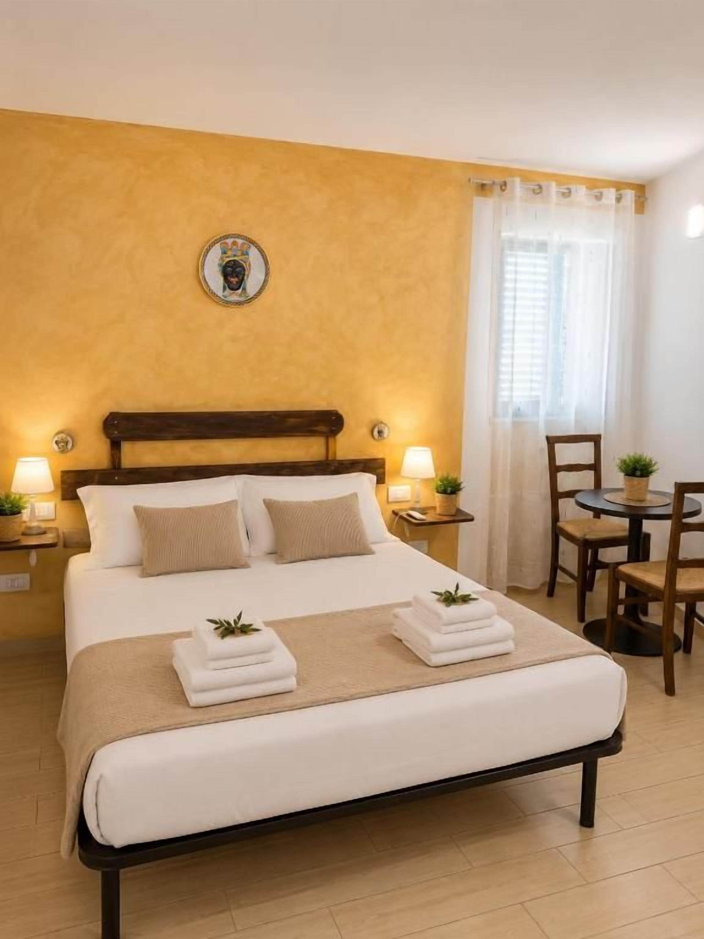 A hotel room with a bed, bedside lamps, a small table, and a chair.