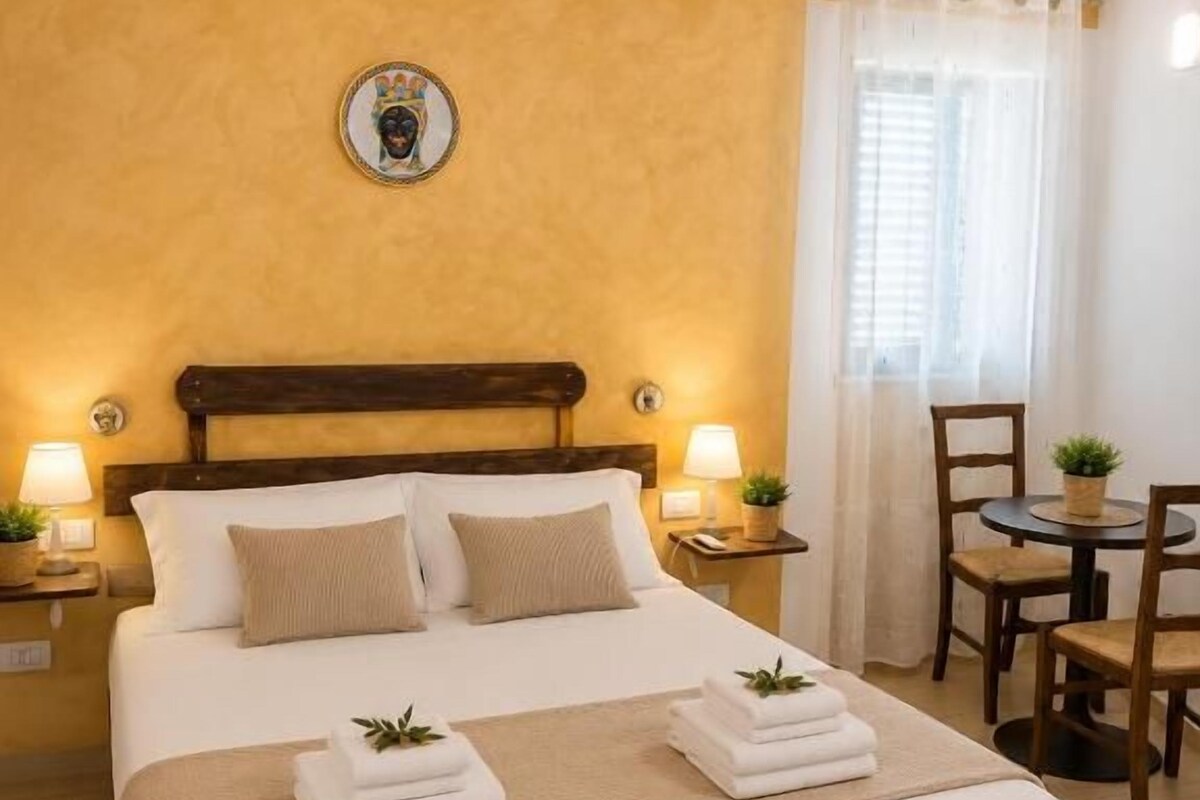 A hotel room with a bed, bedside lamps, a small table, and a chair.