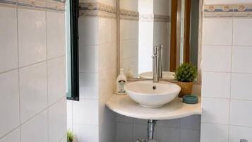 A bathroom with a white sink, a mirror, a small stool, and a bidet.