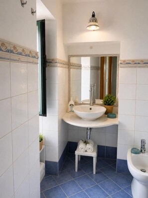 A bathroom with a white sink, a mirror, a small stool, and a bidet. - TELAMON HOME RENT (Agrigento)
