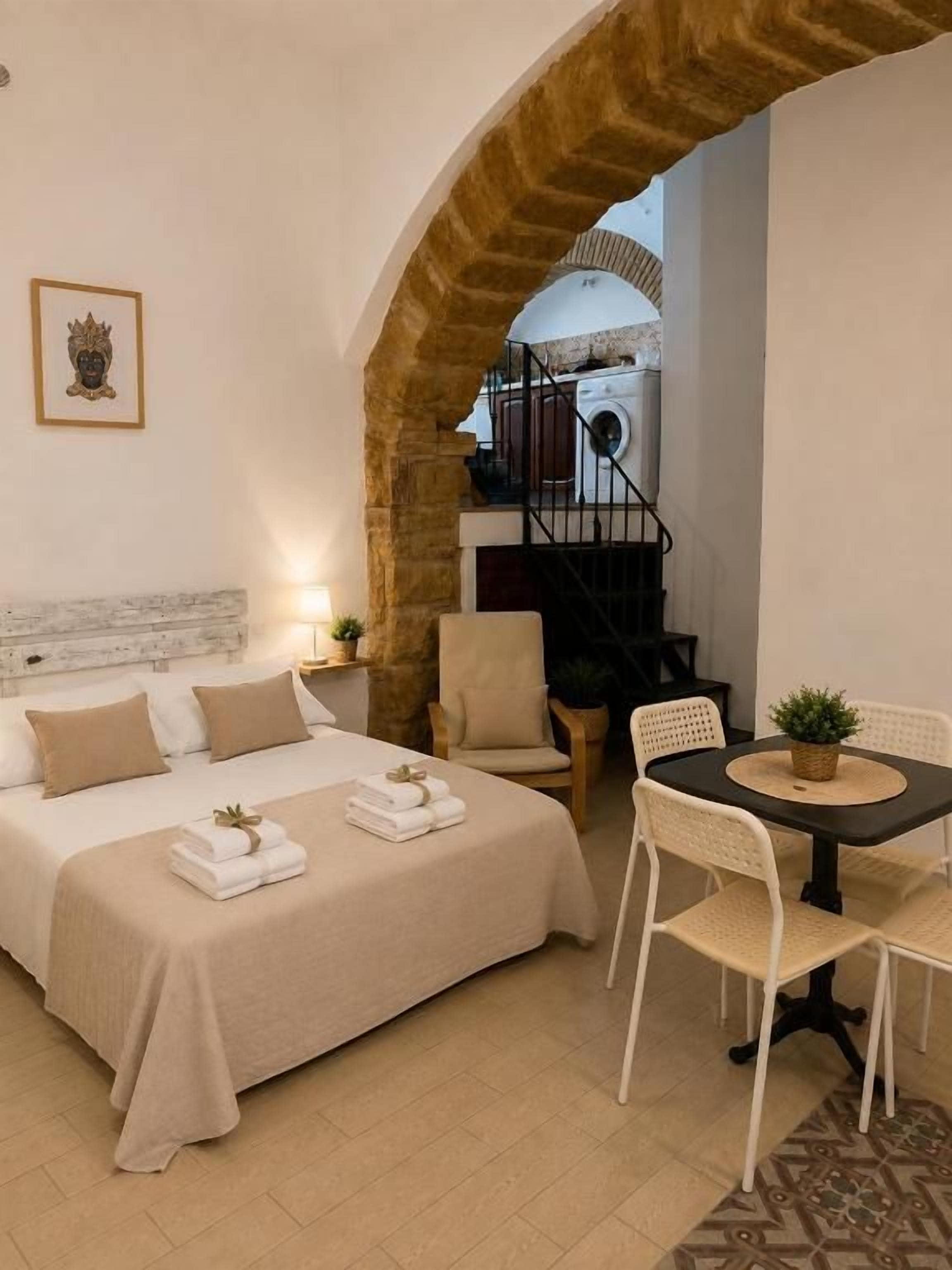 A hotel room with a bed, a dining table with chairs, a small table with a plant, and a staircase leading to an upper level.