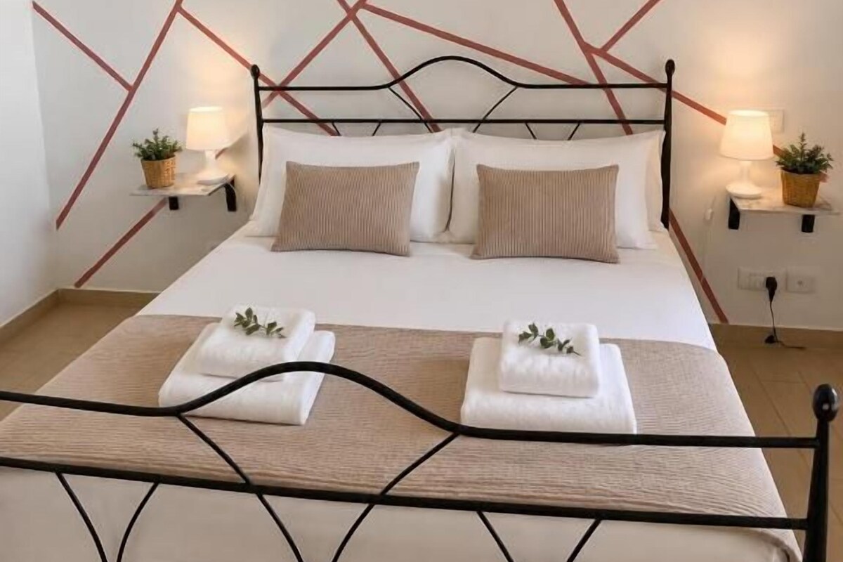 A bed with a geometric wall design, two bedside lamps, and a metal frame.