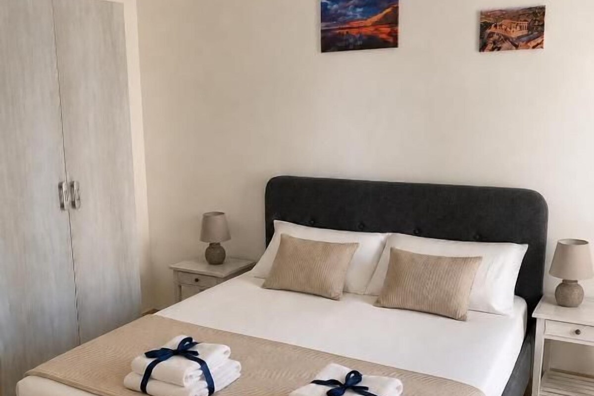 A hotel room with a bed, two bedside tables, a wardrobe, and two wall-mounted artworks.