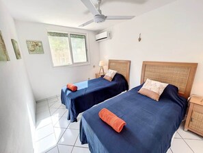 Habitació amb dos llits, ventilador de sostre, aire condicionat i finestra amb persianes.