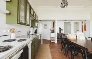 A modern kitchen with green cabinets, a white stove, and a dining area with a wooden table and black chairs. - The Lazy Days Main Cottage - Lakefront (Lambton Shores)